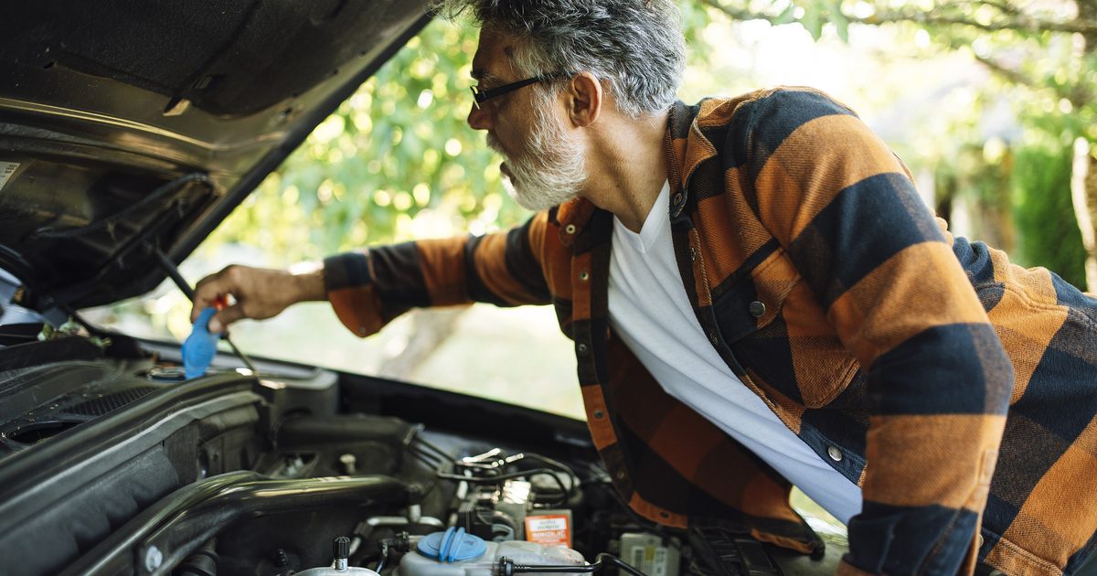 Bărbat care verifică uleiul motorului, aplecat sub capota ridicată a mașinii